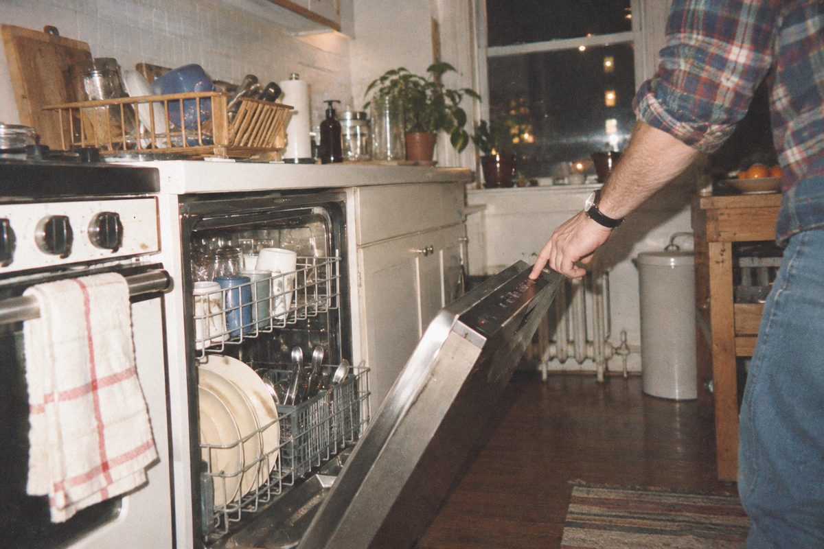 A man reaching to start a loaded dishwasher at night