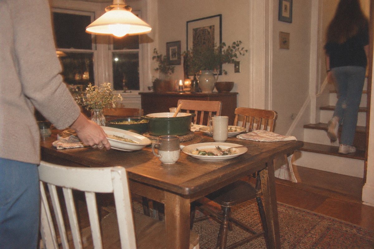 A woman clearing plates as a teenage girl heads upstairs